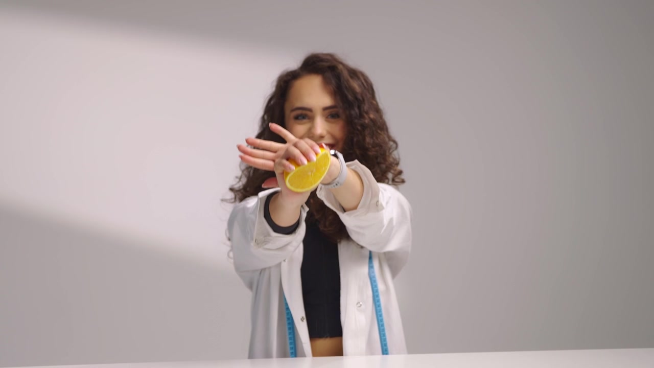 Nutricionista con bata blanca exprime media naranja fresca mientras mira a la cámara. Concepto de estilo de vida saludable con cítricos, bienestar, dieta y nutrición natural sobre fondo blanco limpio