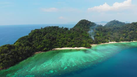 An-aerial-shot-of-a-beautiful-island-with-smoke-coming-from-the-jungle