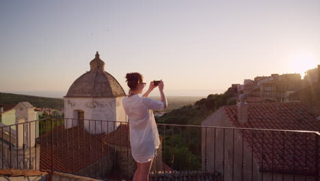 happy woman using smartphone taking photo of beautiful sunset enjoying sharing summer vacation travel experience on balcony