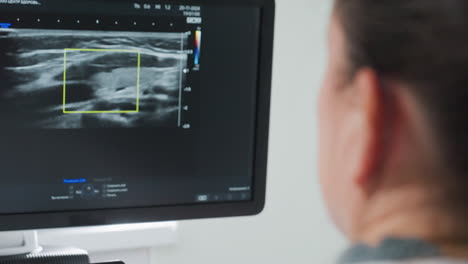 side view of lab technician attentively observing ultrasound machine screen displaying internal body movements during diagnostic procedure, highlighting focused medical analysis and patient imaging