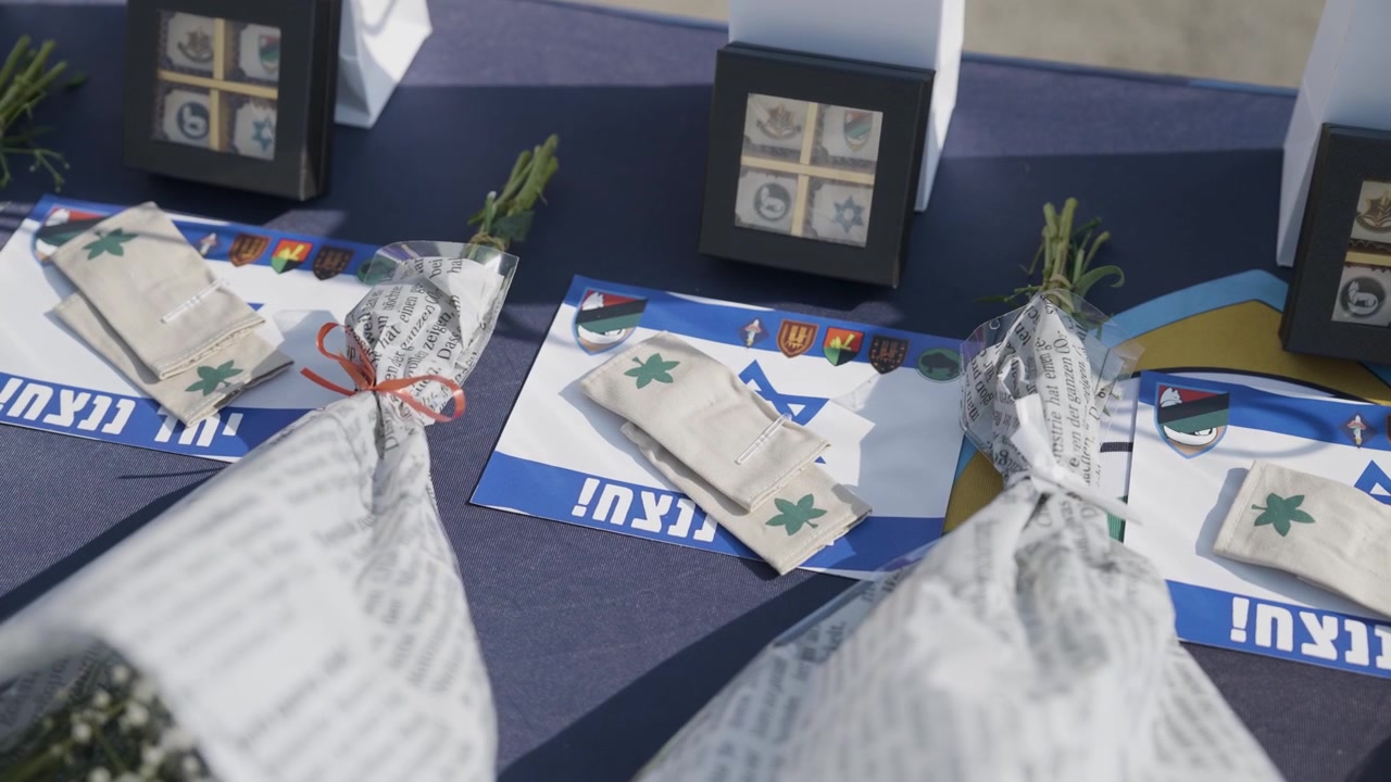 Fila di sacchetti regalo bianchi, premi incorniciati e bouquet di fiori disposti su un tavolo per una cerimonia formale a Gaza, Palestina.