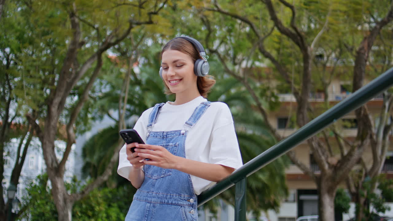 Relaxed hipster listening music in headphones holding phone on street closeup