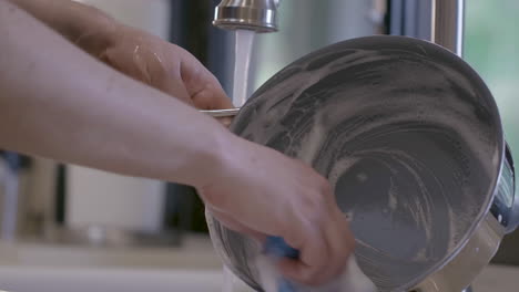 a caucasian male is cleaning a cooking pan in a home kitchen-1