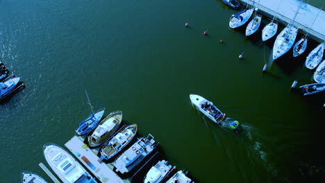 perspectiva aérea de un pequeño barco a motor que se mueve a través del agua cerca de un muelle con varios barcos amarrados en un lado