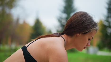close-up of woman in black activewear squatting down, ready to engage in physical activity, blurred background of trees and green foliage, capturing a focused moment before movement