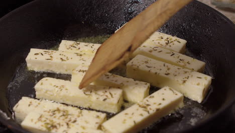 Pieces-of-herb-cheese-are-fried-in-hot-cast-iron-pan,-spatula-stirring