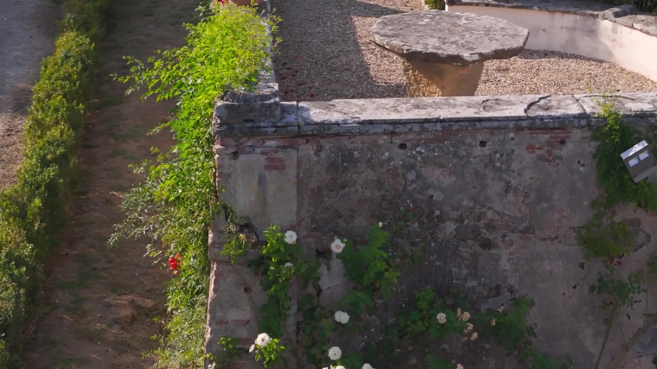 Vista drone che si eleva sopra un vecchio muro di villa in pietra con piante rampicanti e terrazza in ghiaia