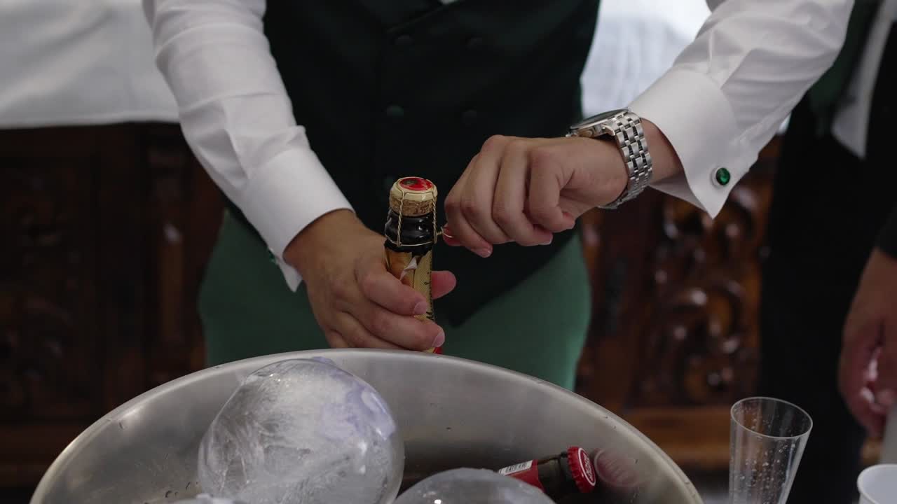Man in formal attire opening a champagne bottle from an ice bucket at a wedding