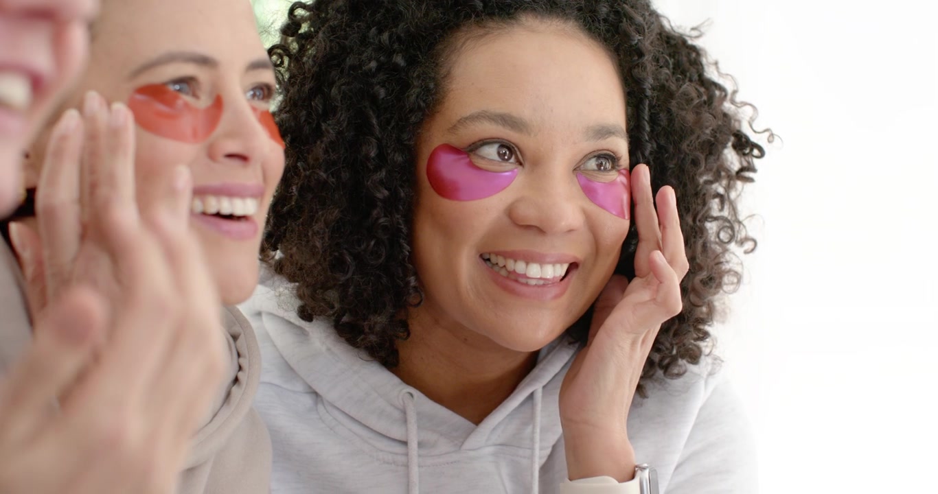 Diverse female friends sitting at home, senior woman speaking, others adjusting under-eye patches
