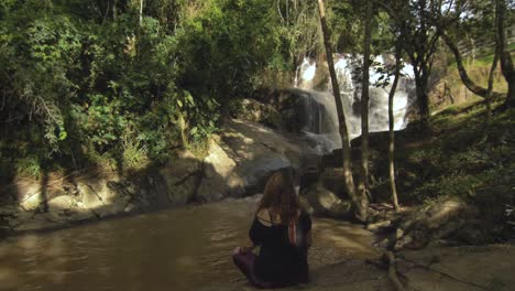woman siting by the waterfall having a meditation during a afternoon time in minas gerais - brazil