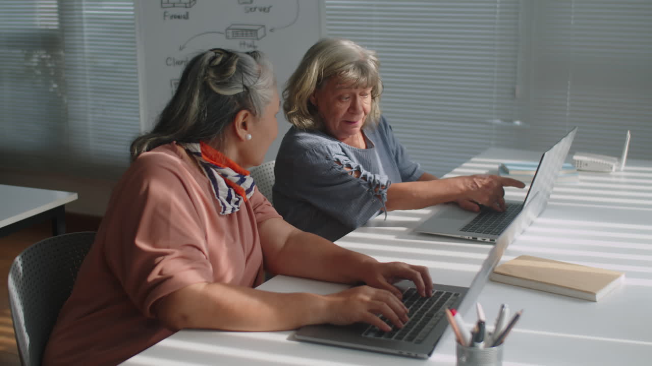 Mature Woman Helping Friend with Laptop during Computer Class