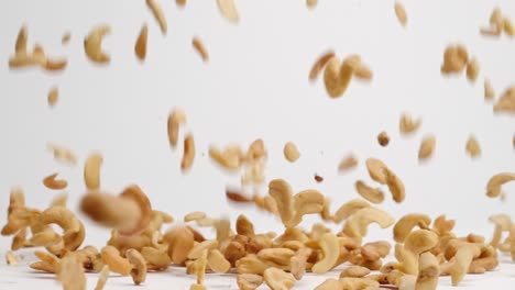 salted, roasted cashew nut halves and pieces bouncing into a pile on white table top in slow motion