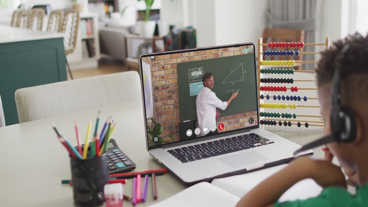 niño afroamericano usando una computadora portátil para una lección en línea con un profesor masculino biracial en la pantalla