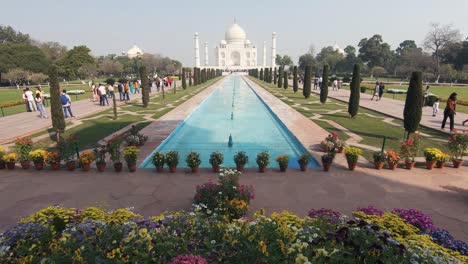 reveal of the main facade of the taj mahal. tourists walk at the gardens.