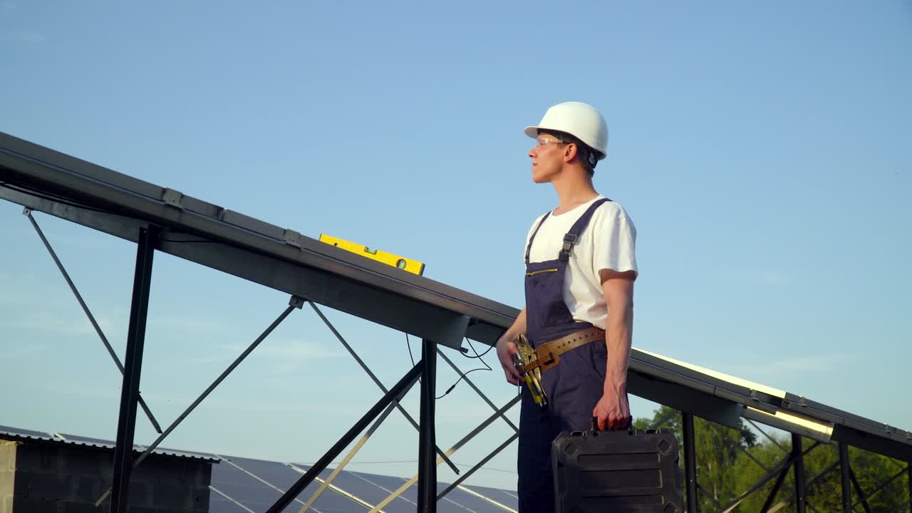 Young enginneer installing new sunny batteries. Worker in a uniform and hardhat installing photovoltaic panels on a solar farm