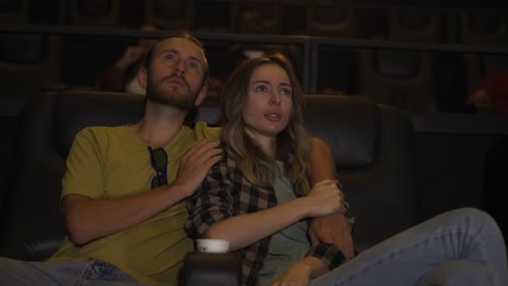 blonde girl looking scary while watching film, her boyfriend calming her down