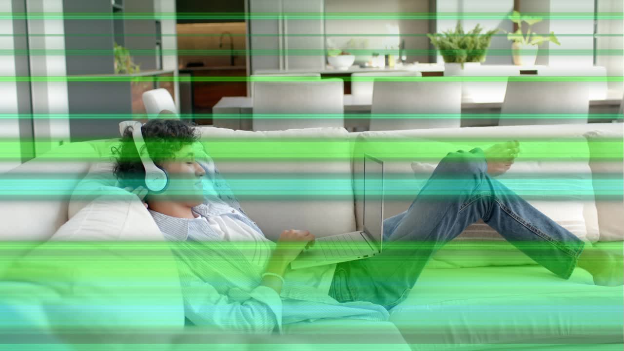 Man lying on sofa typing laptop causing green scans hiding screen while adjusting phones working