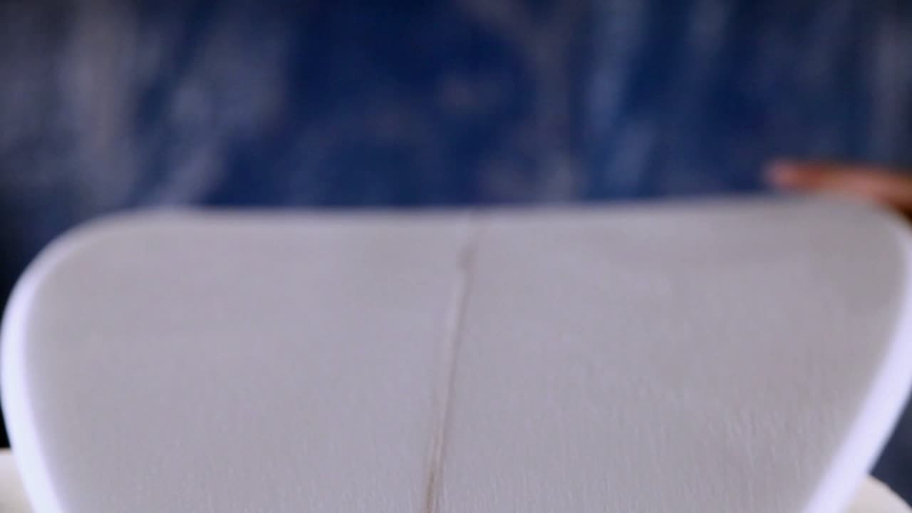 A worker is shaving and cleaning a line through a newly manufactured surfboard