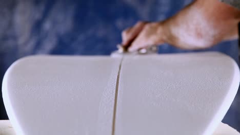 un trabajador se está afeitando y limpiando una línea a través de una tabla de surf recién fabricada
