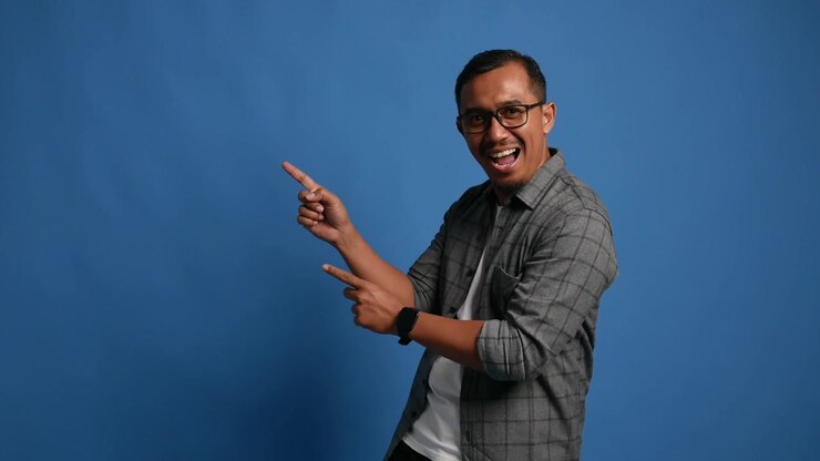 Recommending Asian adult man pointing at right side, copy space. Smiling guy indicates to empty place for your advertising. Male presenting, showing something isolated on blue background.