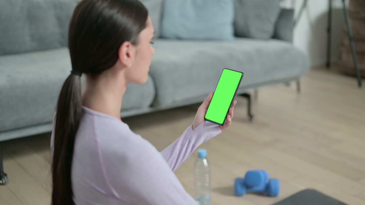 Rear View of Latin Woman using Smartphone with Chroma Screen on Yoga Mat