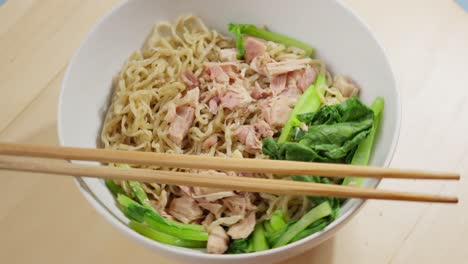 chopsticks on a bowl of bakmi wheat noodles served with bok choy and meat