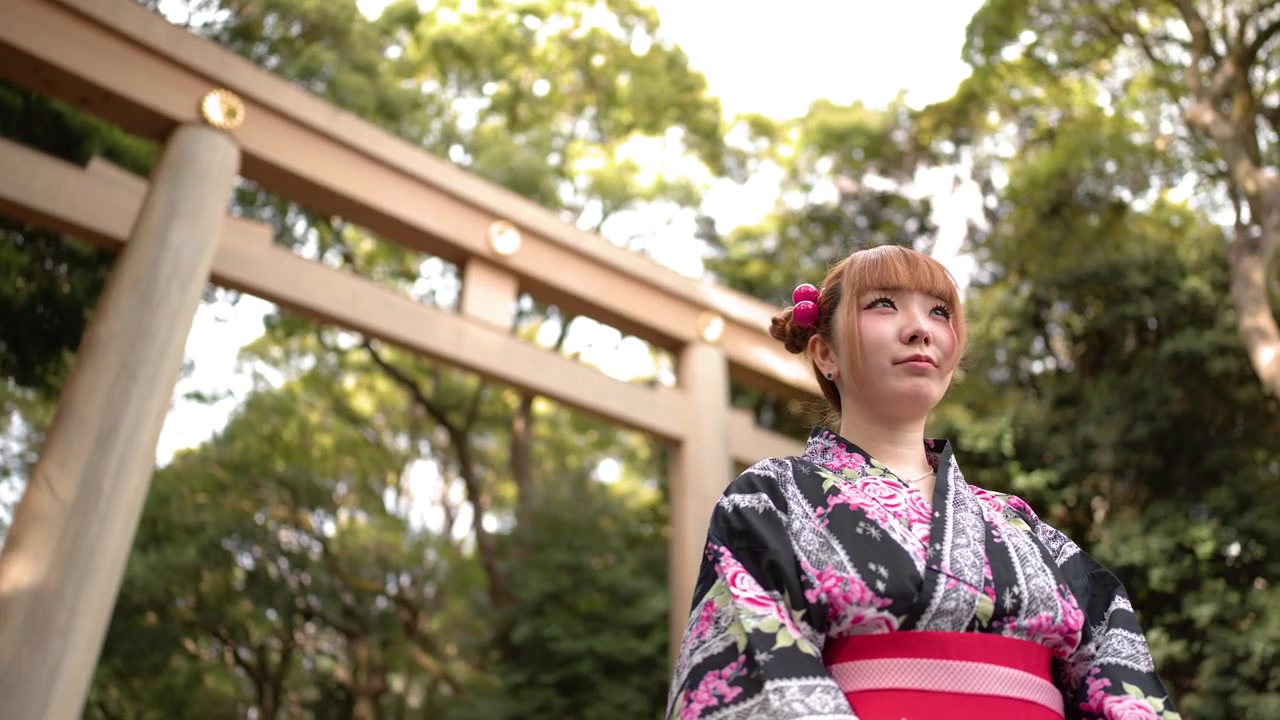 Uma mulher vestindo um yukata floral está em frente a um portão torii de madeira em Tóquio.