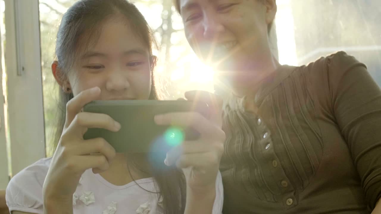 4k 아시아 소녀가 어머니와 함께 스마트폰에서 게임을 하고 행복한 시간을 보내고 있습니다.