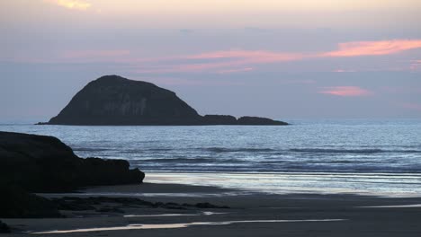 Tranquil-Ocean-With-Mountain-Silhouette-In-Background-During-Sunset-In-Muriwai-Beach,-Auckland,-New-Zealand