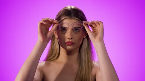 medium shot of a young pretty woman with glasses looking seductively into the camera while taking off her glasses in front of a purple background in slow motion