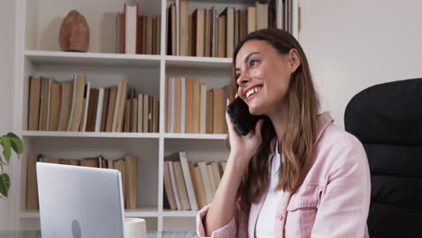 smiling woman talking on smartphone while working from home with laptop, copy space