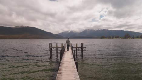 man walks on wooden jetty at lake te anau in new zealand