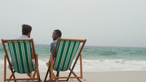 Rear-view-of-Couple-relaxing-on-a-sun-lounger-at-beach-4k