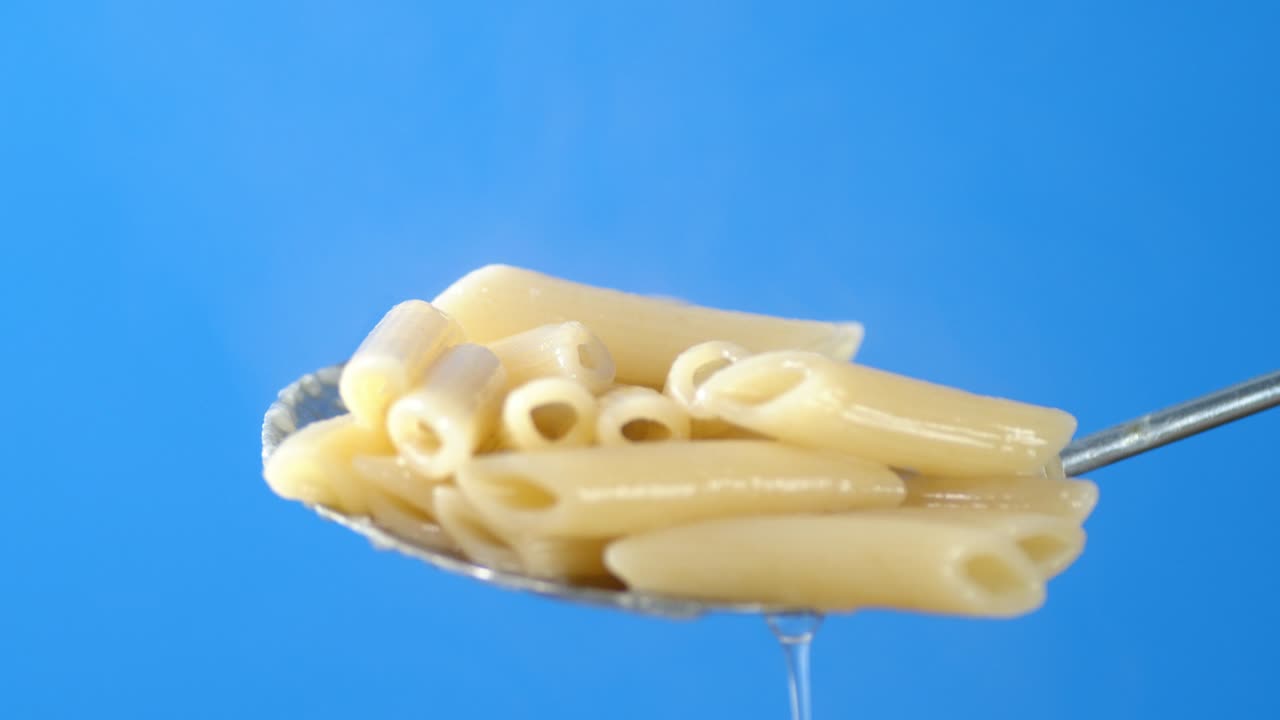 Boiled penne pasta on a spoon with hot steam.