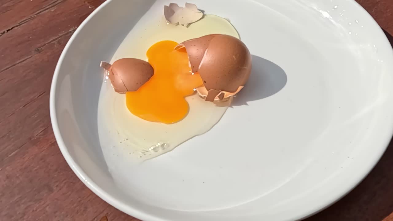 Brown eggs break open, spilling yolk and whites onto a white plate on a wooden surface.