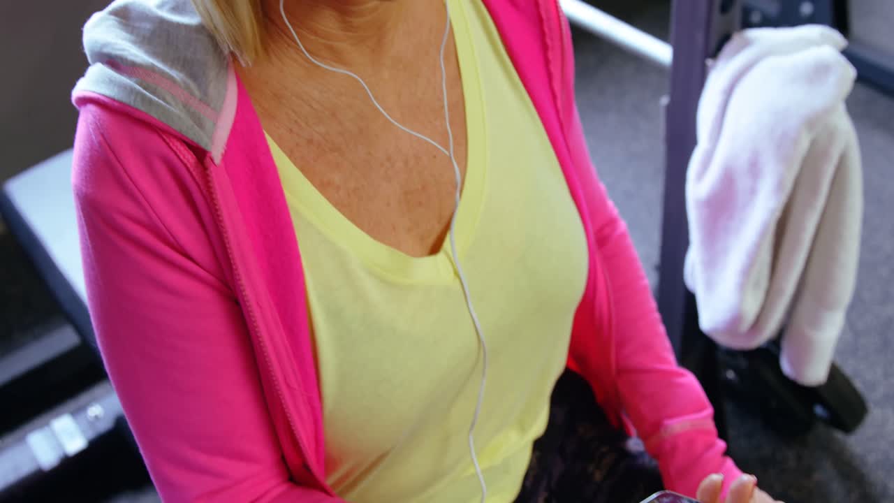 피트니스 스튜디오 4k에서 휴대 전화로 음악을 듣는 고령 여성