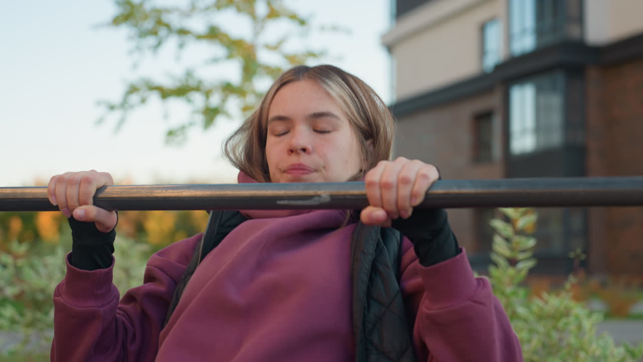 Medium view of female jogger working out on horizontal bars in outdoor park, wearing a hoodie, focused on fitness training with calm background, healthy active lifestyle concept