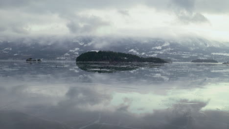 ice fishing at frozen steinsfjorden lake with braksoya island in background in norway