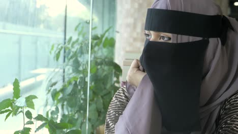 a woman wearing a niqab looks out of a window