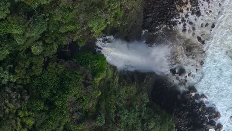 Lush-tropical-landscape-with-waterfall-flowing-into-rocky-coastline-on-Maui-North-Shore