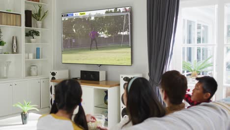 asian family watching tv with african american male soccer player playing match on screen