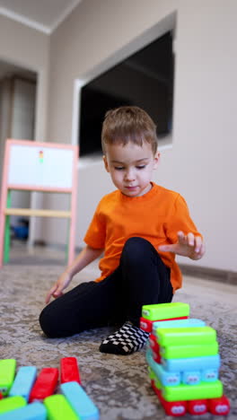 toddler boy sitting on the floor plays with blocks. peaceful caucasian kid builds a tower of bricks. vertical video.