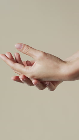 Vertical video of hands of biracial woman on beige background with copy space, slow motion