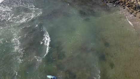 surfer-swims-with-his-board-in-front-of-the-cliff