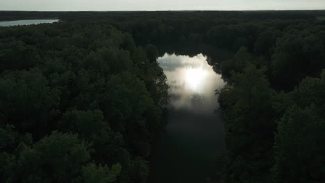 Mesmerizing-river-reflecting-evening-sun,-surrounded-by-dark-mysterious-forest