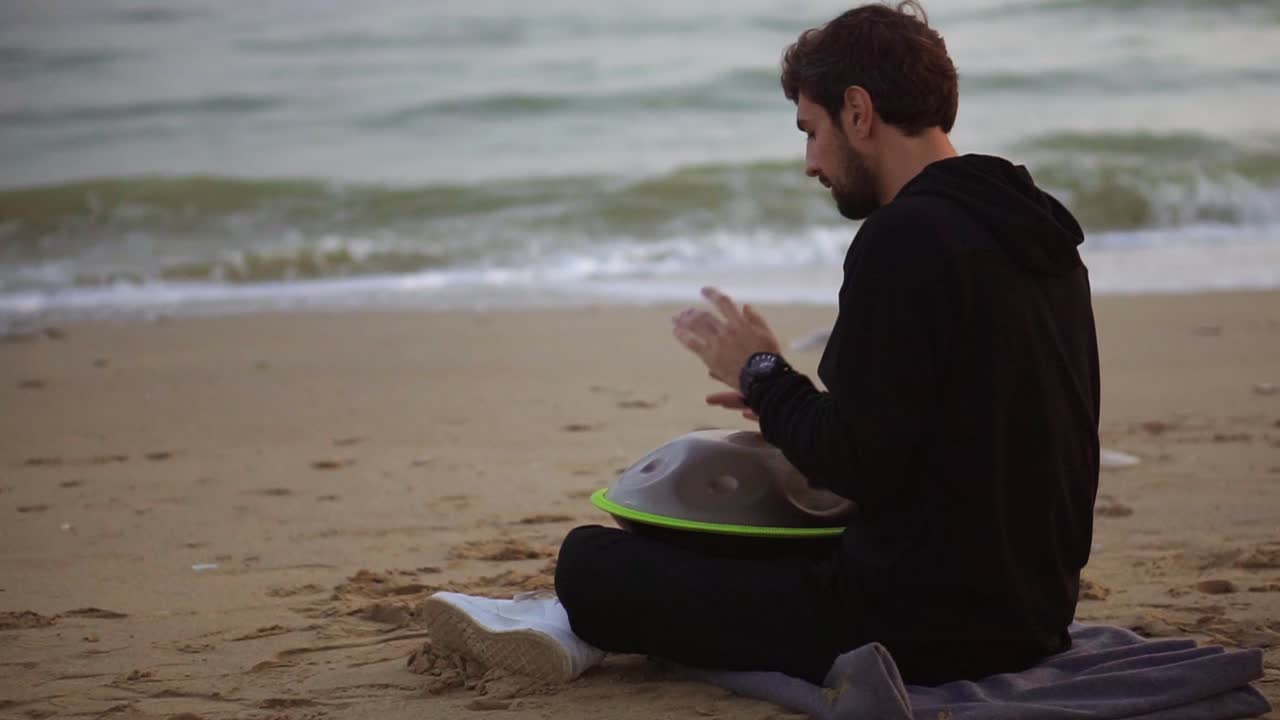el hombre de negro casual jugando colgar sentado en la playa frente al mar solo en otoño