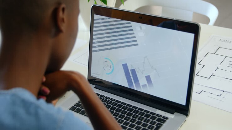 Rear view of young black businesswoman sitting at table and working on laptop in modern office 4k