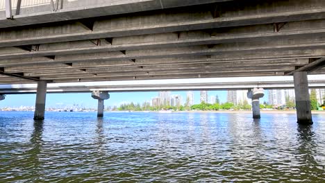 boat travels under bridge with city skyline view