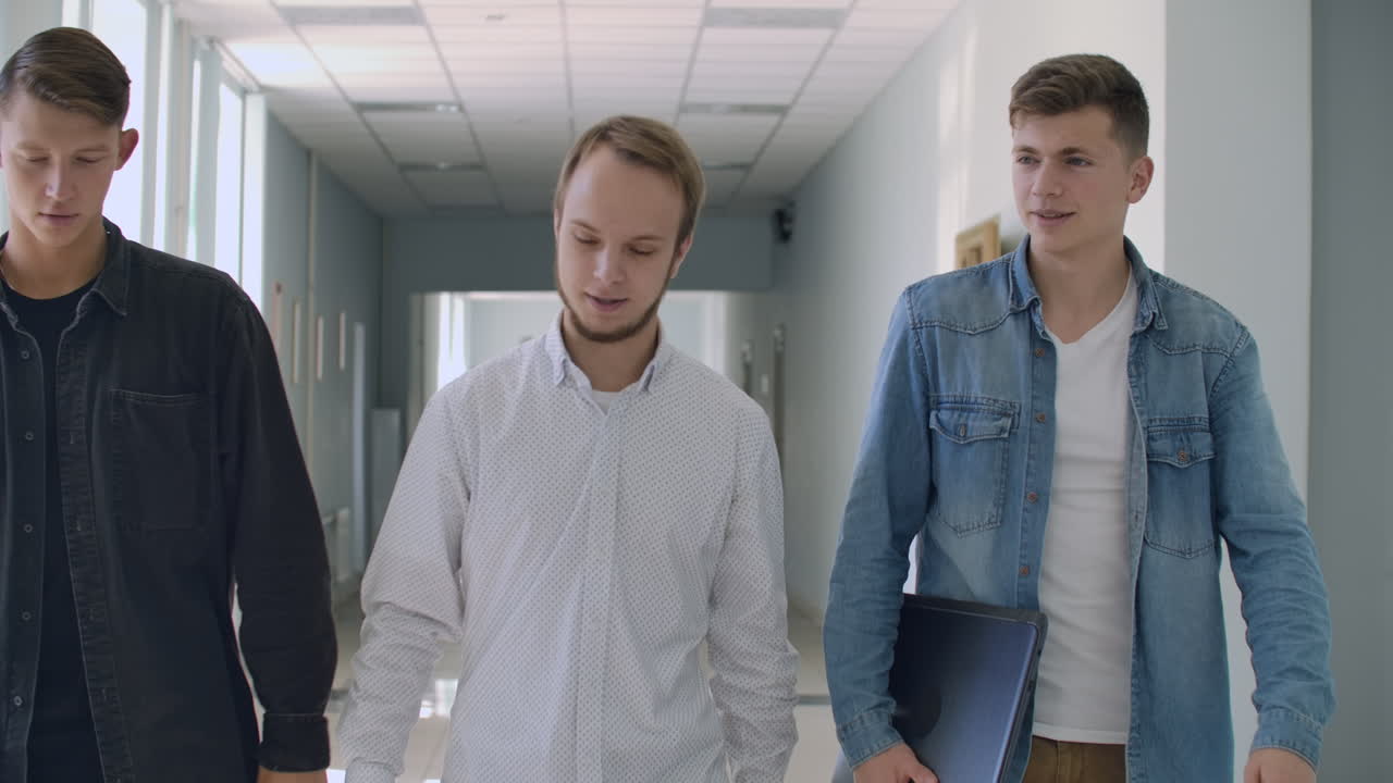университетские коридоры в колледже. трое мужчин идут и весело смеются и говорят о школе и о девушке. институт и ежедневное общение в колледже, молодежь