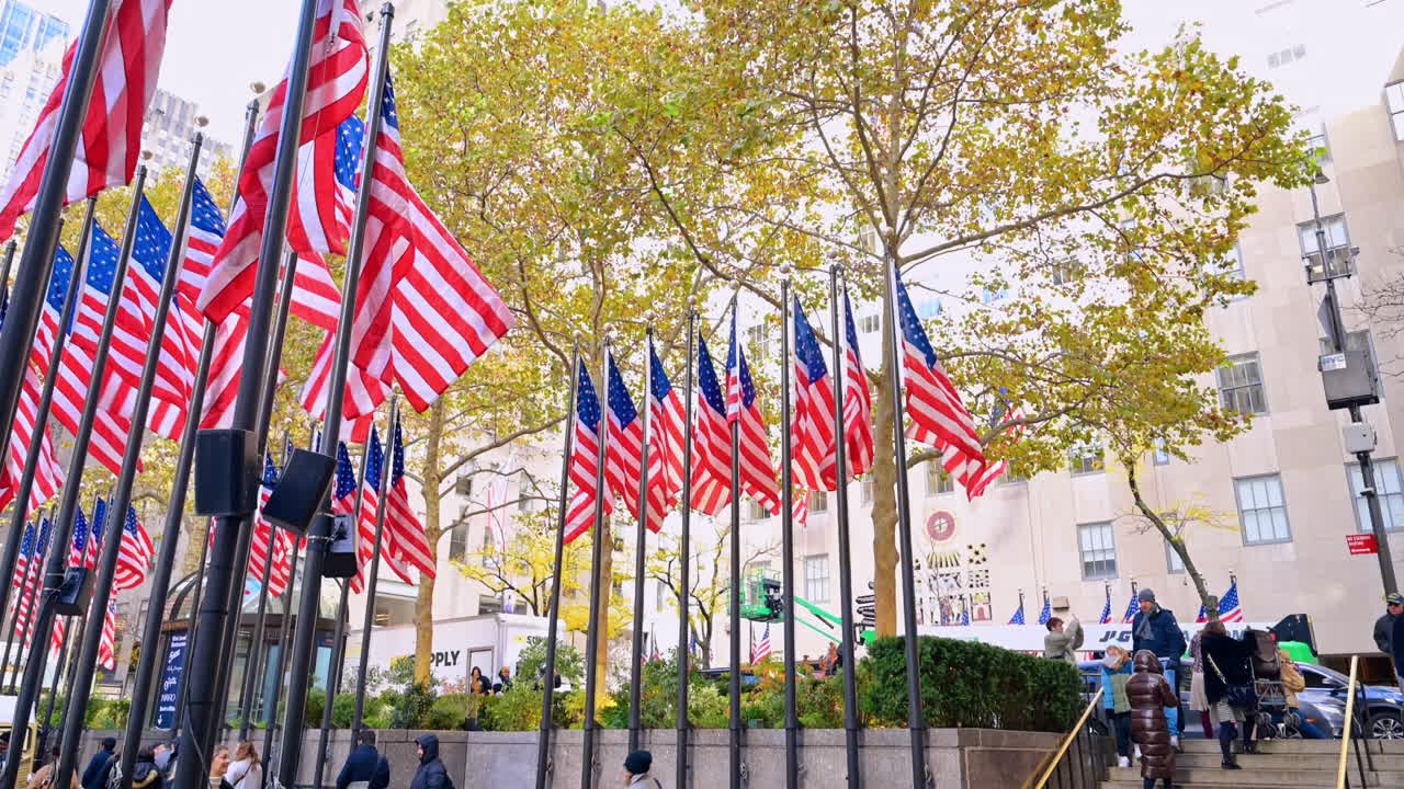 New York, USA, 8 November 2025: People walking near Rockefeller flag. People walk past the American flag display in the vibrant Rockefeller Center plaza
